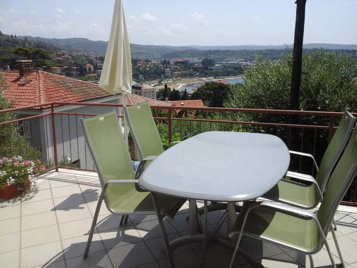 Terasa apartmaja 1 z mizo, stoli in senčnikom, zadaj Portorož in zaliv
